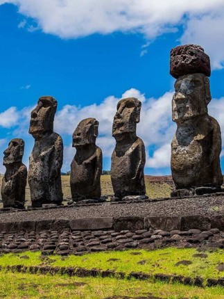 A row of towering Moai statues stands on a stone platform under a bright sky on Chile's Easter Island. 