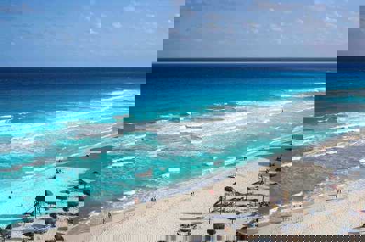 Sweeping view of Cancun's turquoise waters and white-sand beach lined with sun loungers and umbrellas. 