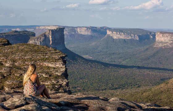 Woman sitting on cliff edge with panoramic views of mountains in Chapada Diamantina National Park, Brazil. 