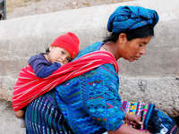Central America - Guatemala, Indigenous mother carries child in traditional woven clothing, reflecting daily life and culture. 