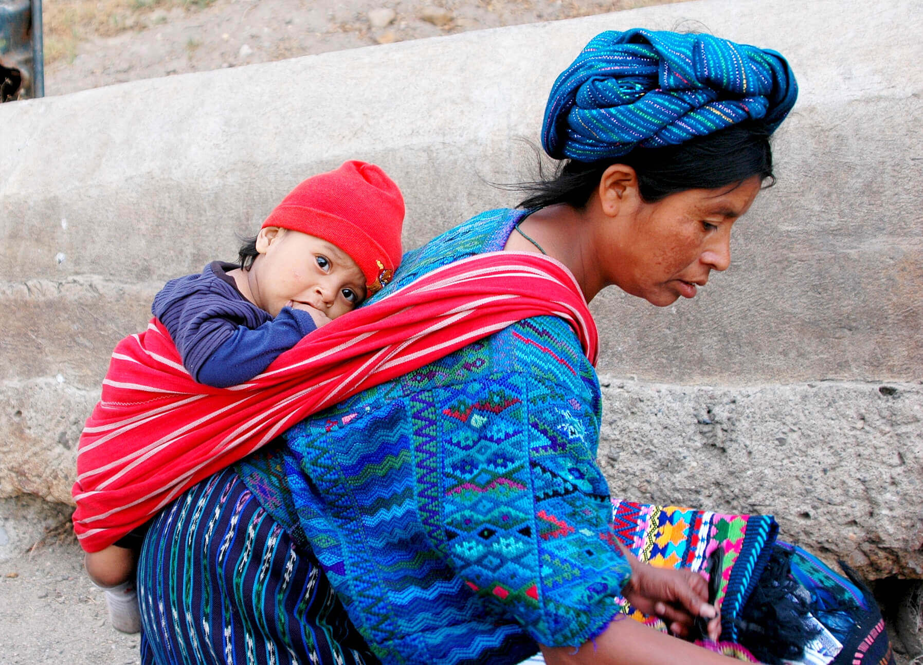 Central America - Guatemala, Indigenous mother carries child in traditional woven clothing, reflecting daily life and culture. 