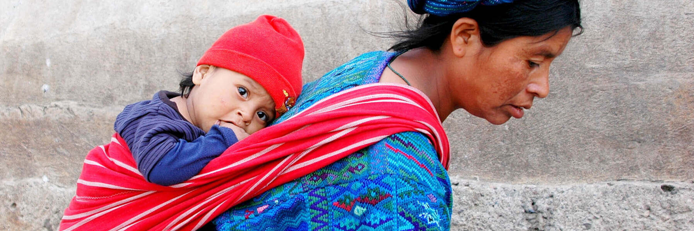Central America - Guatemala, Indigenous mother carries child in traditional woven clothing, reflecting daily life and culture. 