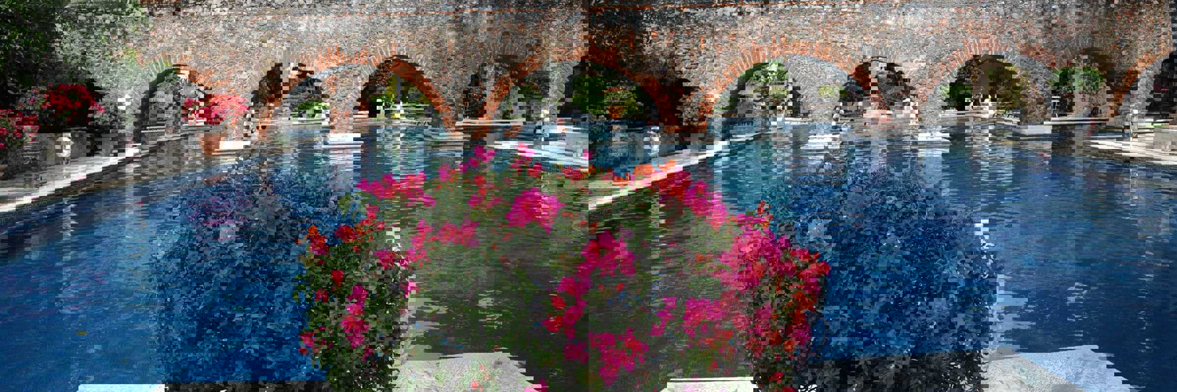 Charming Mexican hacienda with a serene pool, stone arches, and vibrant flowers in a tranquil garden setting. 