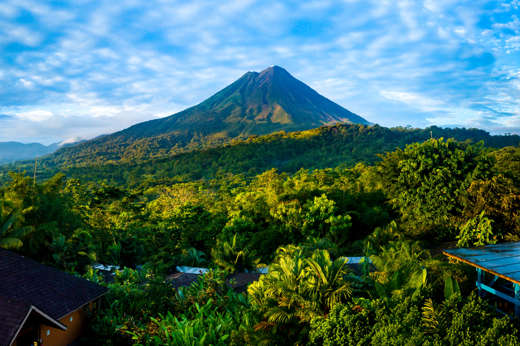 Arenal Volcano rises above the tropical forest of Costa Rica, framed by colorful lodges. 