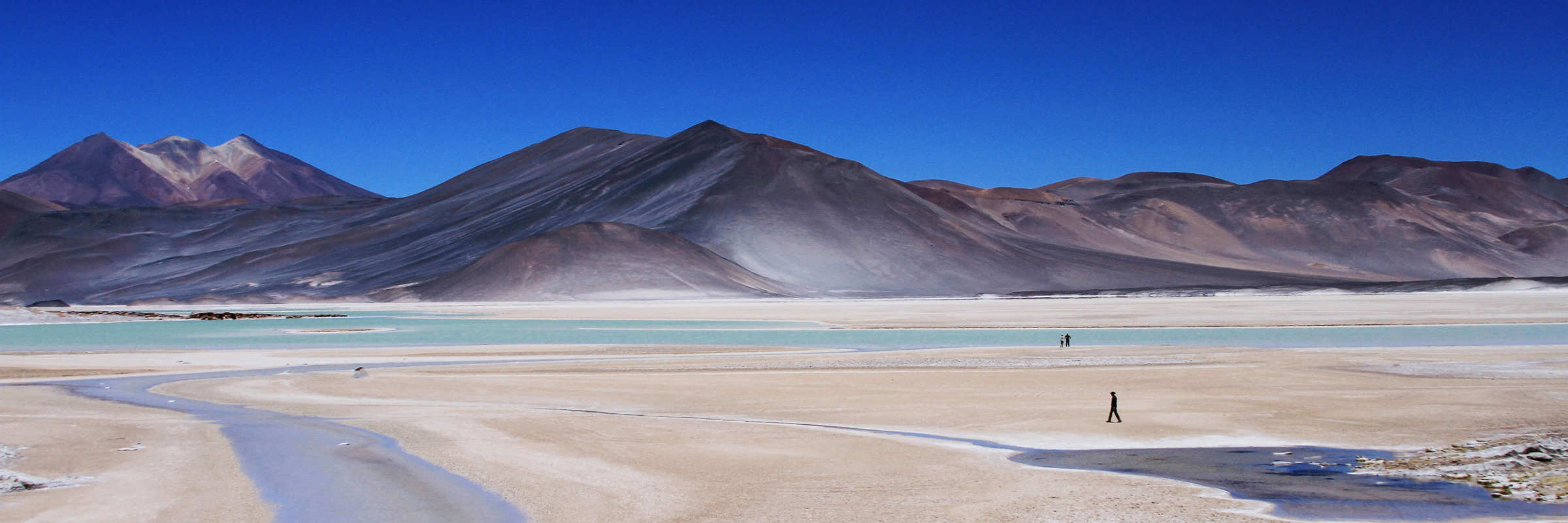 Vast salt flats with volcanoes in the distance under a deep blue sky in the Atacama Desert. 