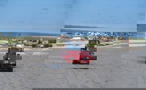 Red beach buggy driving across sand dunes in Jericoacoara with ocean and coastal town in the background.