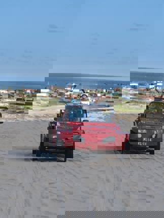 Red beach buggy driving across sand dunes in Jericoacoara with ocean and coastal town in the background.